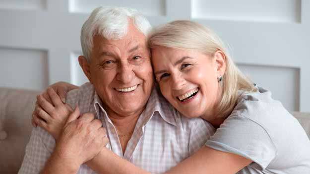 Smiling elderly couple sitting on a couch, the man displaying his new dentures.