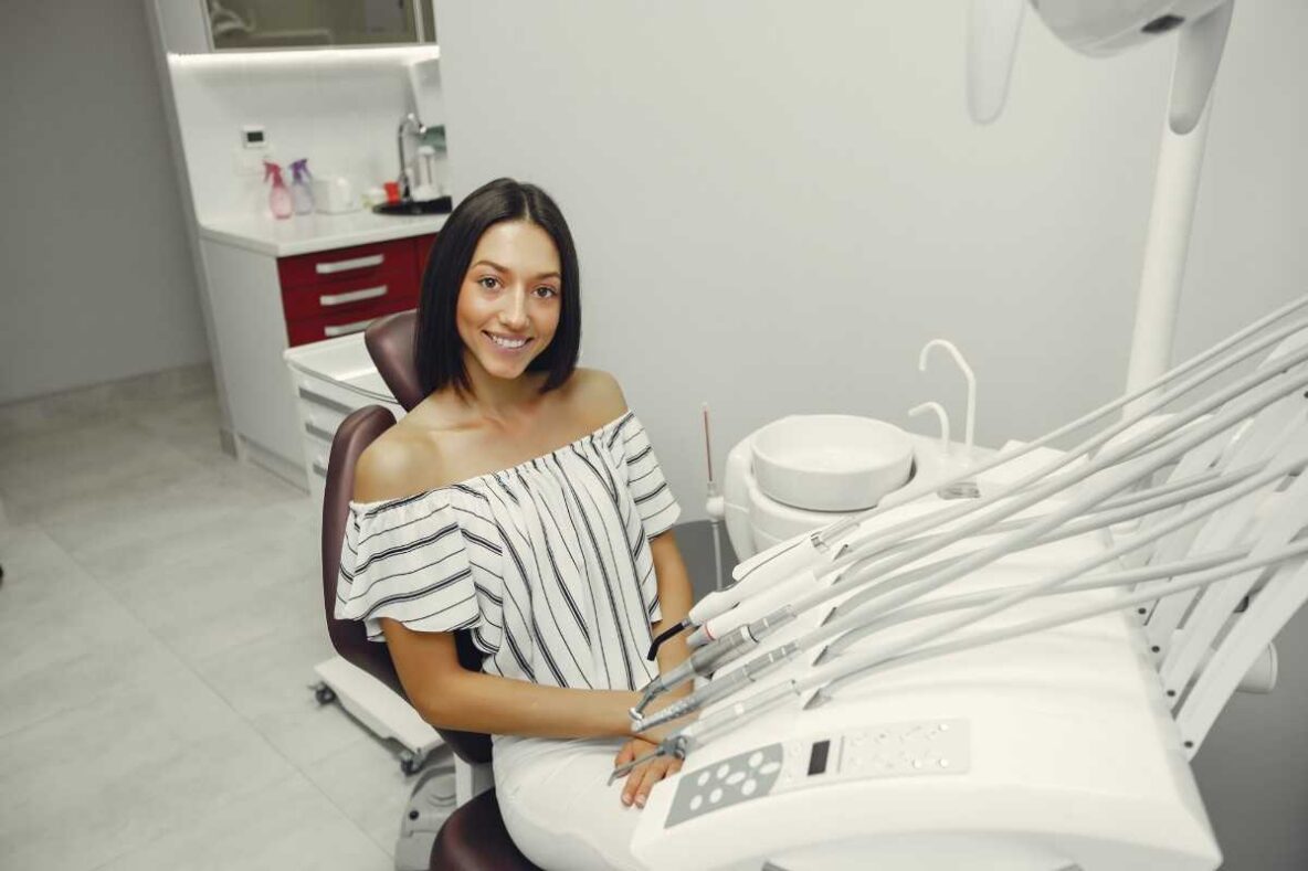 Dentist showing a dental model to a smiling female patient seated in a dental chair during a consultation.