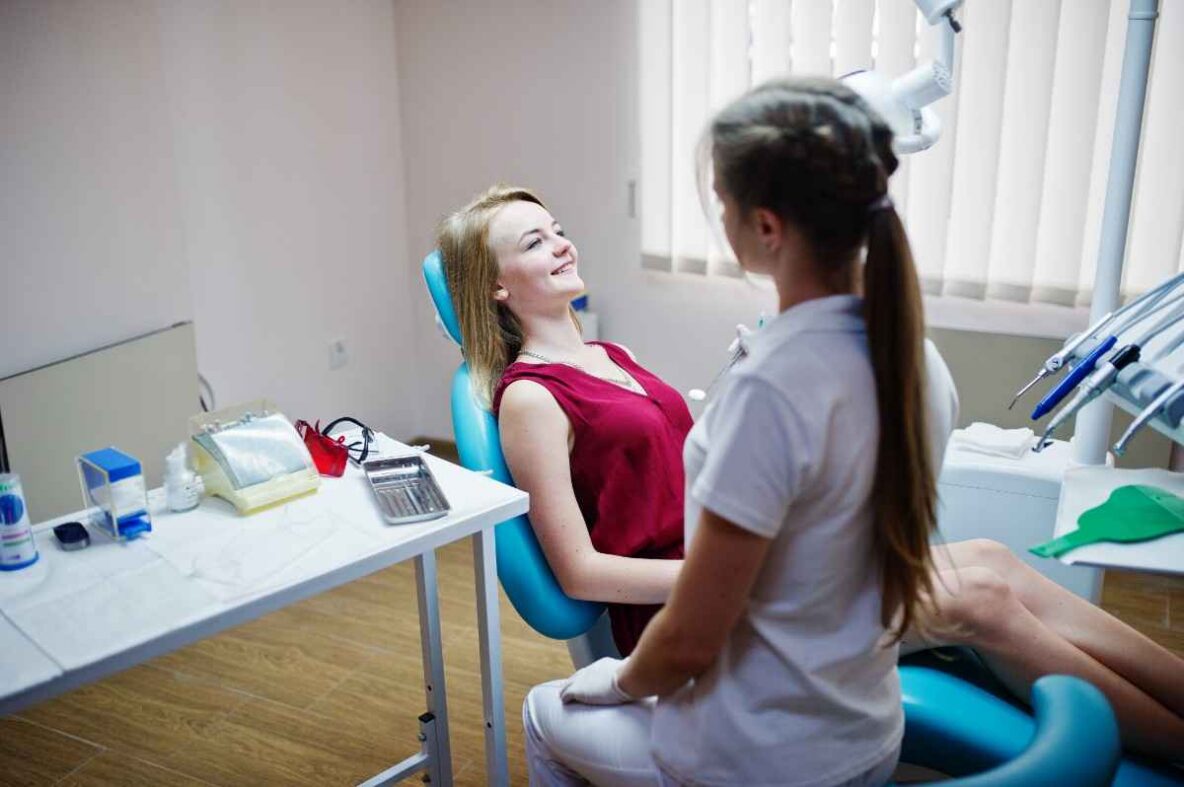 Dentist showing a clear dental aligner model to a female patient seated in a modern dental clinic.